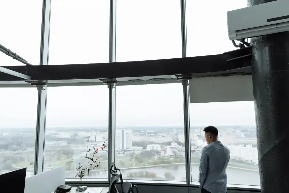 An executive stands alone at an office window after hours, head bowed, after a difficult day of decisions.
