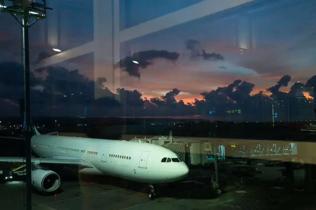 A business executive sits alone at an airport window at dusk watching planes against a wide sky.