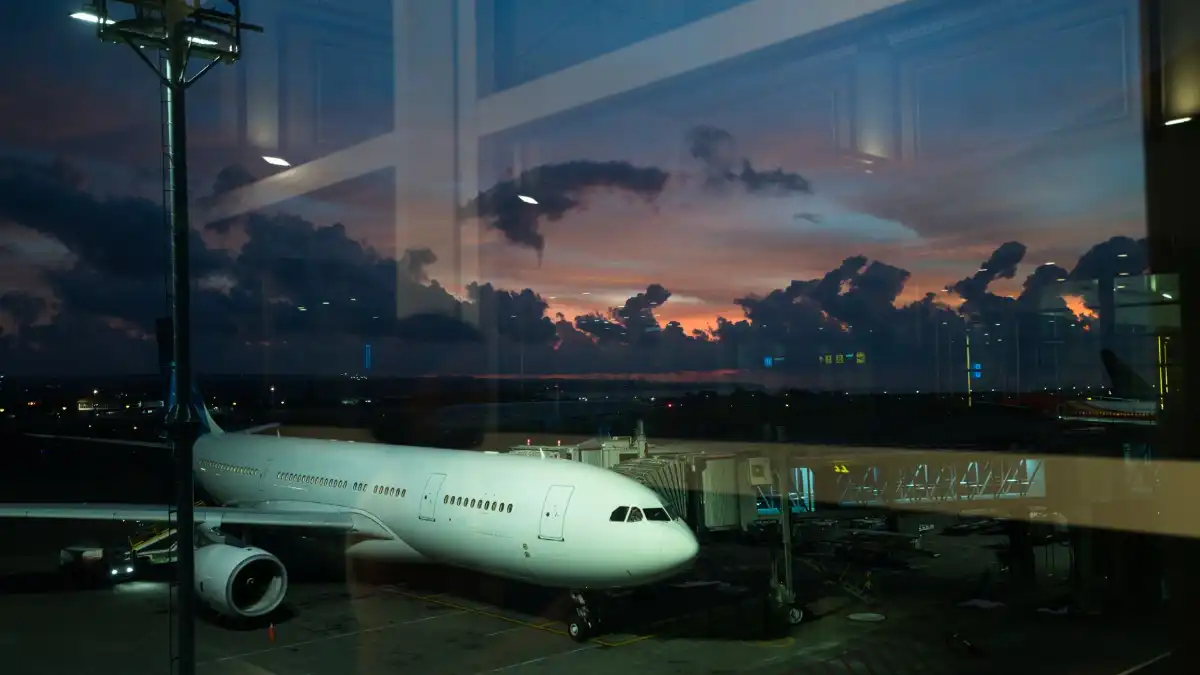 A business executive sits alone at an airport window at dusk watching planes against a wide sky.