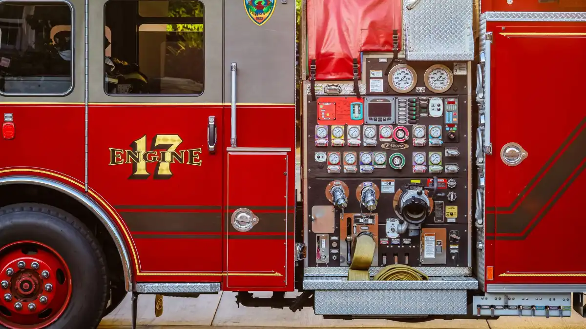 A fire chief stands alone at dusk before a quiet fire station with engines visible behind him.