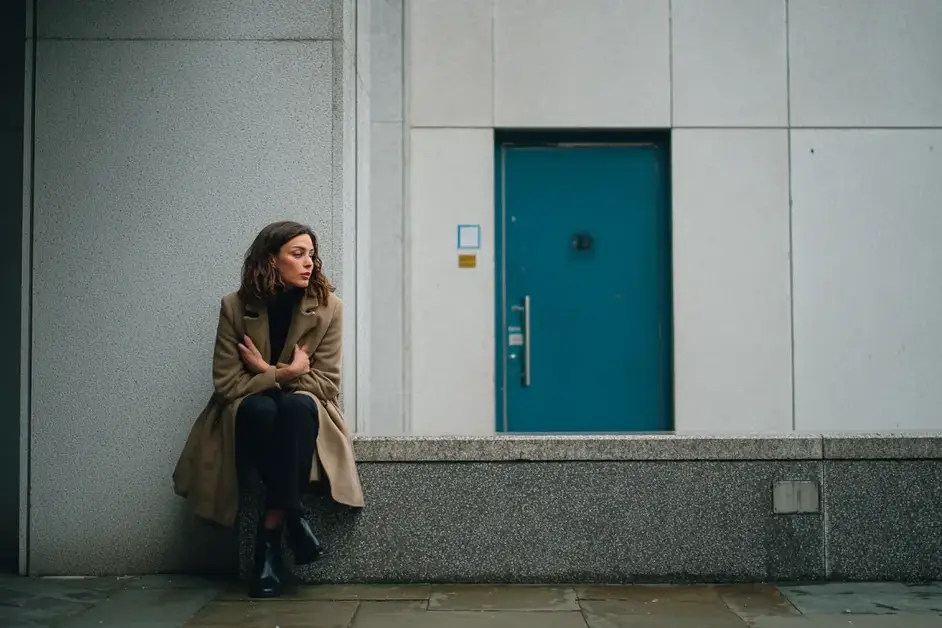 Woman sitting against the outside wall of an office building with one hand flat against her chest