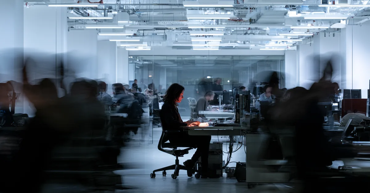 Long-exposure photo of a still, focused office worker surrounded by blurred, rushing colleagues